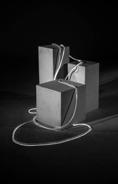 Siyah-beyaz bir fotoğraf, geometrik blokların tek bir parlayan kabloyla zarif bir şekilde bağlandığı bir sanat kurgusu sergiliyor. Metin için boşluk.