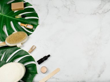 Doğal kaplıca ürünleri, masaj fırçası, deniz tuzu ve beyaz arka planda tropik canavar yaprakları..