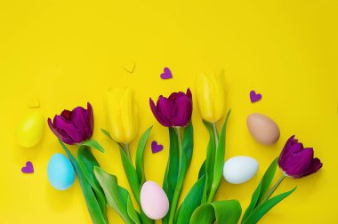 Sarı arka planda bir buket lale ve Paskalya yumurtaları..