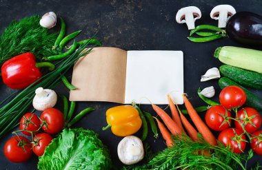 Koyu arkaplanda taze sebzeler, yemek tarifleri için bir defter..