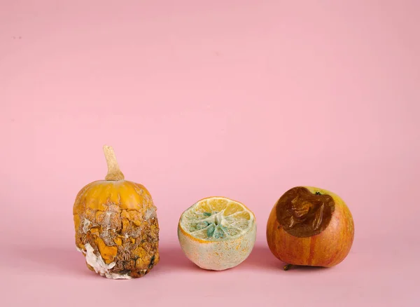 Rotten missing pumpkin, lemon, apple on pink background.