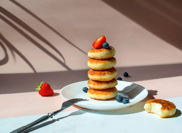 Cottage cheese pancakes with strawberries and blueberry on a pink background with shadows. Breakfast or lunch concept. — Stock Photo, Image
