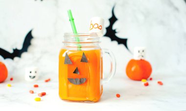 Cadılar Bayramı için iç. Hildrenler ve Cadılar Bayramı ziyafetleri. Gözlüklü balkabağı portakalı kokteyl, beyaz mermer bir masada ürkütücü yüzler ve korkunç şekerlemelerle süslenmiş. Boşluğu kopyala