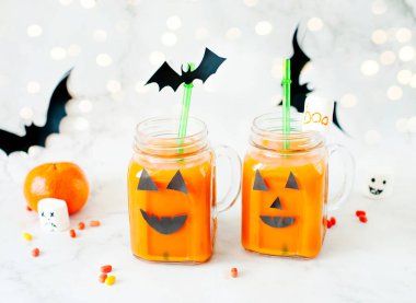 Cadılar Bayramı için iç. Hildrenler ve Cadılar Bayramı ziyafetleri. Gözlüklü balkabağı portakalı kokteyl, beyaz mermer bir masada ürkütücü yüzler ve korkunç şekerlemelerle süslenmiş. Boşluğu kopyala