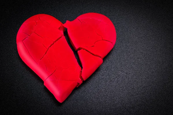 Broken and broken red heart on a black background. Closeup. Vignette. Valentine's Day.