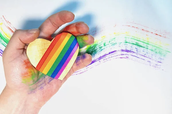 lgbt sembollü bir kalbi tutan adamın eli. Arka planda gökkuşağı çizilmiş. Özgür aşk. Lezbiyen Gey Biseksüel Transseksüel. Sevgililer Günü.