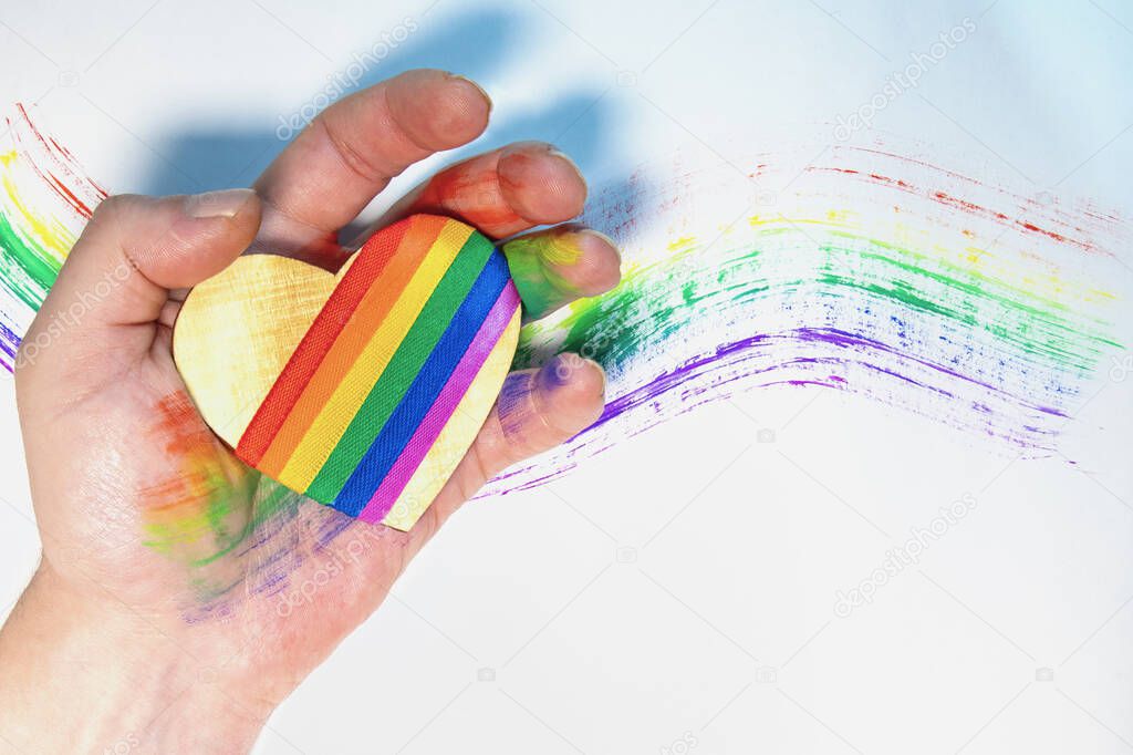 Man's hand holding a heart with lgbt symbols. Drawn rainbow in the background. Free love. Lesbian Gay Bisexual Transgender. Valentine's Day.