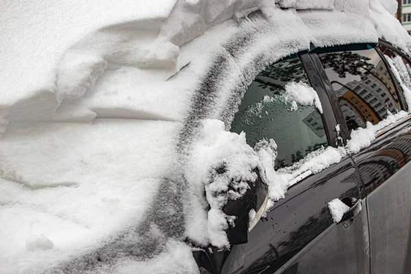 Snow-covered frozen car covered with snow. Winter road. Danger of winter driving. Car snow removal. Dangerous traffic situation.