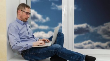 İş adamı pencerenin kenarında dizüstü bilgisayarla oturuyor ve monitöre bakıyor.