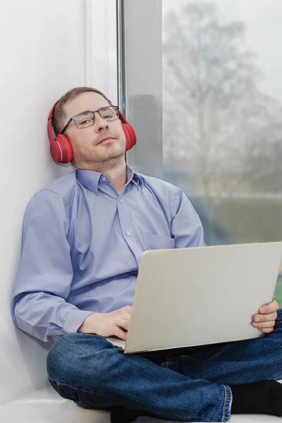 Hombre Sienta Alféizar Ventana Con Auriculares Portátil Relajación Escuchar Música —  Fotos de Stock