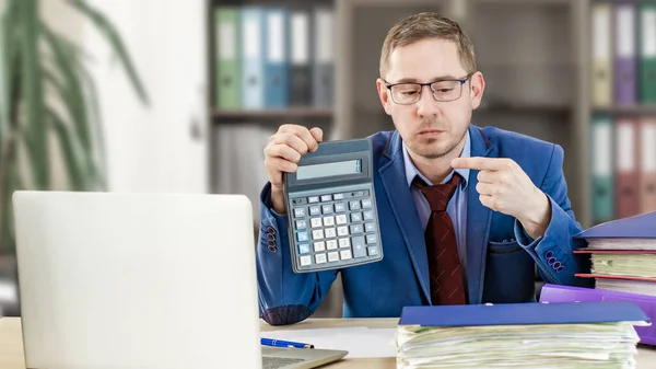 Accountant businessman at his desk in the office shows a finger on a calculator. Financial check. Preparation of a report by an office worker
