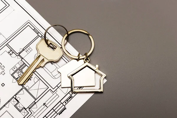 The concept of mortgage and rental housing and real estate. Mortgage credit lending. Metal keychain in the shape of a house with a key on the plan of the house. Buying a house