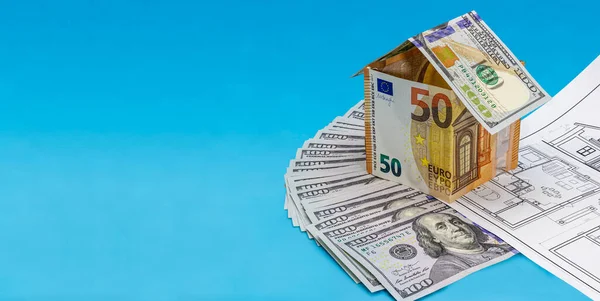 The concept of mortgage and rental housing and real estate. Mortgage credit lending. House of euro bills on the plan of the house and laid out dollar banknotes on a blue background. Banner format