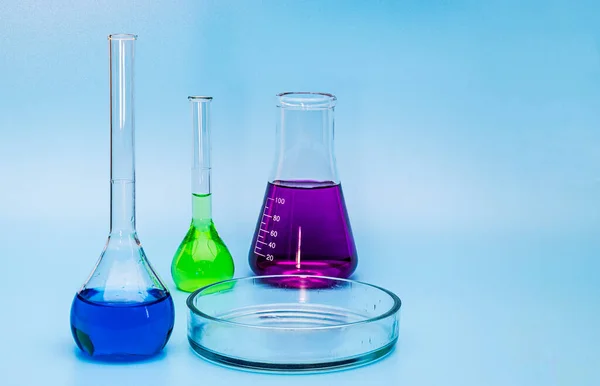 Three glass medical laboratory flasks with different multi-colored liquids and a glass bowl on a gentle blue medical background. The concept of medical and chemical experiments. Close-up. copy space