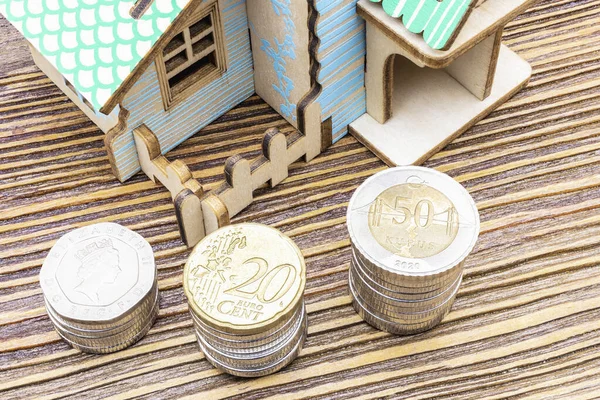 The concept of mortgage, sale and rental of housing and real estate. Buying a home. A mock house with stacks of coins in the foreground on a wooden surface. Banner format. Copy space