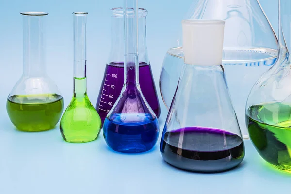 青の背景に異なる色の液体と異なるサイズのガラス医療研究所のフラスコ 実験室のチューブと装置 実験室実験の概念 — ストック写真