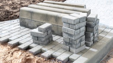 Asfalt tamiri ve kaldırım taşlarının döşenmesi, arka planda fayans küplerinin istiflenmesi. Şehrin yaya bölgesine kaldırım döşeme döşemesi, kum dolgu. Yol fayansları ve kaldırımlar