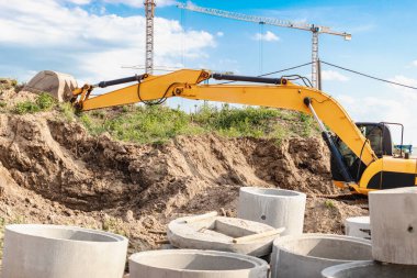 Bir kazıcı, bir konut inşaatı için bir temel kazıyor. Arka planda yeni binalar var. İnşaat üretimi. Kazı