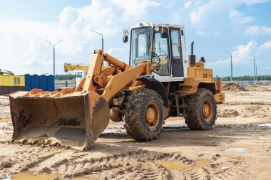 İnşaat alanında elinde kova olan ağır bir yük taşıyıcı. Toprak işçileri, taşımacılık ve malzeme yükleme ekipmanları - toprak, kum, ezilmiş taş