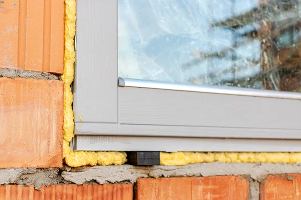 Installation of a window in a brick building. Industrial engineering. Darkening and installation of a window opening using polyurethane foam