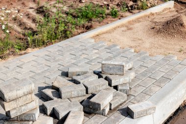 Asfalt tamiri ve kaldırım taşlarının döşenmesi, arka planda fayans küplerinin istiflenmesi. Şehrin yaya bölgesine kaldırım döşeme döşemesi, kum dolgu. Yol fayansları ve kaldırımlar