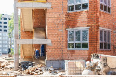 Kırmızı tuğlalı çok katlı bir bina inşa ediliyor. Bir ev inşa ederken iskelenin kullanılması. Sanayi ve sivil inşaat. İnşaat güvenliği