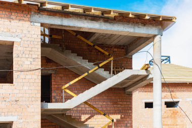 Kırmızı tuğlalı çok katlı bir bina inşa ediliyor. Bir ev inşa ederken iskelenin kullanılması. Sanayi ve sivil inşaat. Güçlendirilmiş beton merdiven