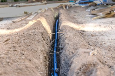 Yerdeki bir sipere mavi bir elektrik kablosu döşemek. Yeraltı iletişimi. İnşaat alanında elektrik işi.