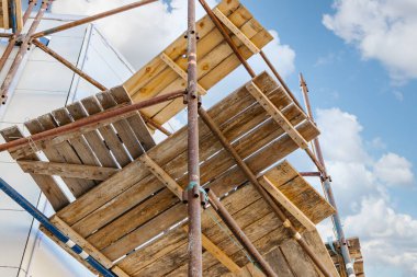 Mavi gökyüzüne karşı tahta güvertelerle iskele ve iskele. Yükseklerde inşaat işi yapıyor. İnşaat güvenliği