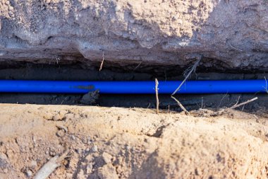 Yerdeki bir sipere mavi bir elektrik kablosu döşemek. Yeraltı iletişimi. İnşaat alanında elektrik işi.