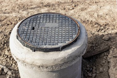 Beton bir kuyuya metal bir kapı döşemek. Yakın plan. Yol çalışıyor. Yeraltı tesislerinin ve kuyularının korunması