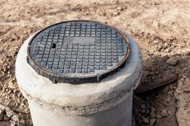 Installation of a road metal hatch in a concrete well. Close-up. Road works. Protection of underground utilities and wells clipart