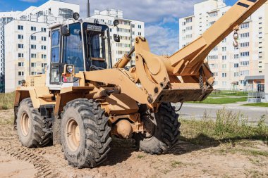 Modern bir yerleşim alanının şantiyesinde ağır malları taşımak için güçlü bir tekerlek yükleyici. Yükleri kaldırmak ve taşımak için inşaat ekipmanları