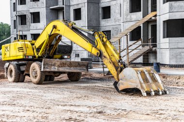 Büyük bir kova ile ağır bir sürüngen kazıcısı inşaat halindeki bir panelin önünde çalışmaya hazırlanıyor. Toprak işçiliği için ağır inşaat malzemeleri. Taş ocağı kazıcısı