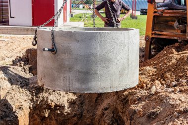 Kazı makinesinin hidrolik piston sistemi çelik kablolardaki beton kanalizasyon şebekesinin çukuruna iniyor. Kanalizasyon evinin inşaatı veya onarımı
