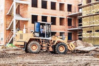 İnşaat alanındaki bir forklift güçlendirilmiş beton levhayı kaldırır. İnşaat makinesi. Tuğla bina ve mineral yünlü termal yalıtım.