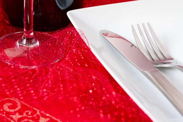 White place setting with glass and bottle on red net cloth — Stock Photo, Image