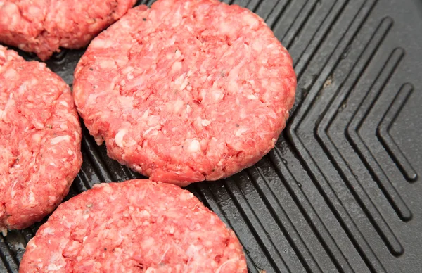 Raw burgers on a metal griddle — Stock Photo, Image