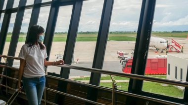 Tramvay bagajlı Asyalı turist, havaalanı terminaline giderken salgını önlemek için hijyenik maske takıyor. Coronavirüs sonrası yeni normallik, covid-19 virüs salgını