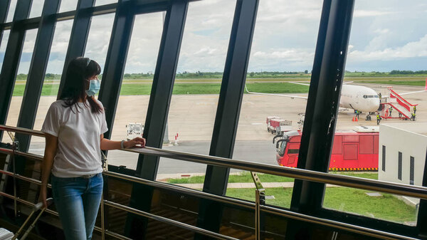Asian tourist with trolley luggage ,wearing hygienic mask to prevent pandemic during travel at airport terminal. new normal after coronavirus, covid-19 virus epidemic