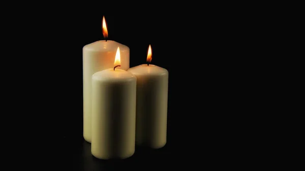Three burning candles glow in the dark