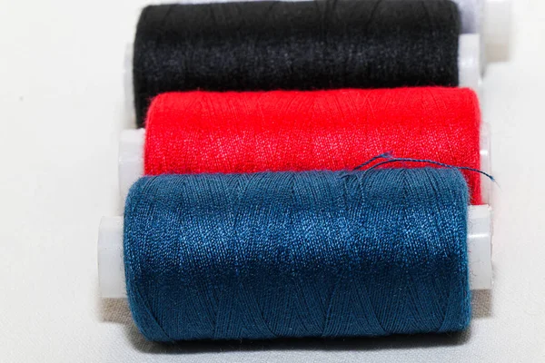 Renkli iplikler ve iğneler. Dikiş için gereken her şey. Birkaç iplik makarası. Keskin iğneler. Kırmızı, siyah, gri ve mavi iplik bobinleri beyaz arkaplanda izole edilmiş.