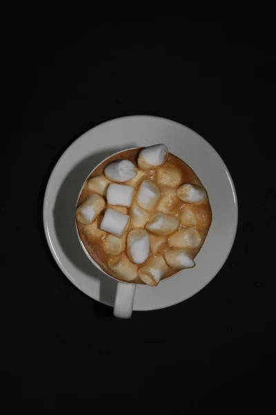 Black coffee with a white cup on a white platter, sprinkled with marshmallow isolated on a black background