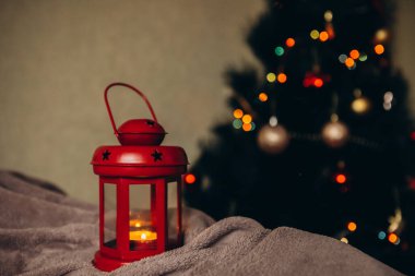 Noel ağacının arka planında kırmızı renkli kırmızı bir Noel feneri ve çelenkleri. Noel ve Yeni Yıl kavramı
