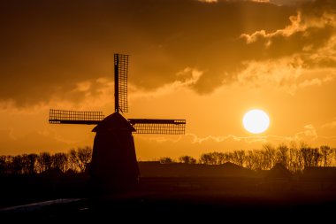 backlit Dutch windmill during sunrise clipart