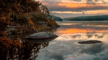 Gölün kayalık kıyısı ve sudaki günbatımının yansımaları.