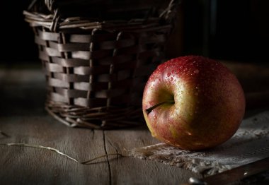 Kırsal bir masada, koyu bir duvarın arka planında duran ıslak kırmızı elma.