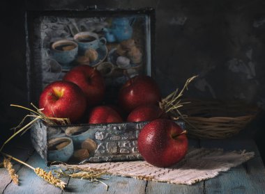 Kırsal bir masada mavi bir mücevher kutusunda su damlatan kırmızı elmalar.