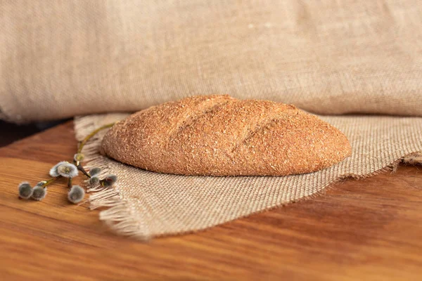 Tahta arka planda kepekli taze ev yapımı ekmek, çuval bezi ve söğüt filizi. Yemek fotoğrafı..