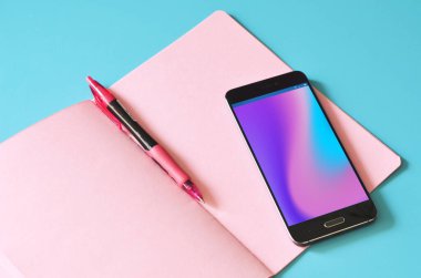Akıllı telefon ve pembe defter mavi masada.. 